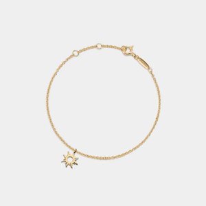 Gold bracelet with a sun-shaped charm on a light gray background