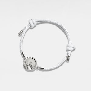 White leather bracelet with silver sun locket on a light gray background