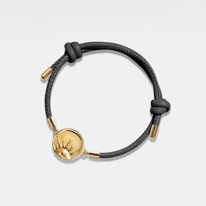 Black leather bracelet with gold sun locket on a light gray background