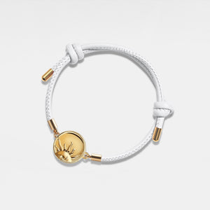 White leather bracelet with gold sun locket on a light gray background