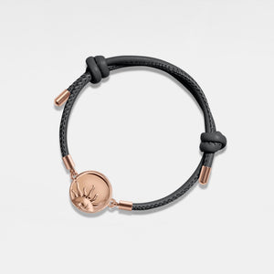 Black leather bracelet with rose gold sun locket on a light gray background