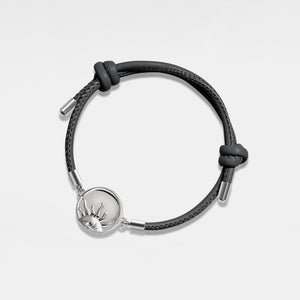 Black leather bracelet with silver sun locket on a light gray background