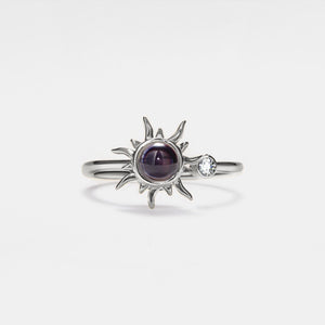 Silver projection ring with sun design and gemstones on a light gray background