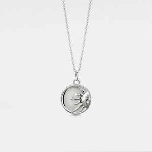 Silver necklace with a round locket feature a sun face design on a light gray background