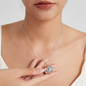 Sterling silver round locket necklace worn on a model, shown open to reveal a photo insert inside, held gently by hand.