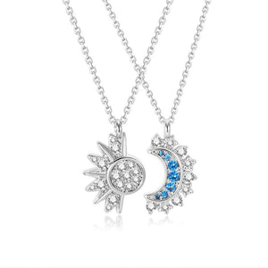 Two necklaces with celestial themed pendants, one with a sun design and the other with a moon design, both adorned with small blue and clear stones, set against a white background.