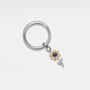 Silver projection keychain with a gold sunflower charm on a light gray background