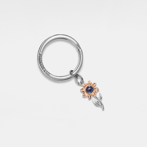 Silver projection keychain with a rose gold sunflower charm on a light gray background