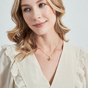 A model wearing a gold-plated sterling silver necklace with a sunflower charm and a central projection stone, displayed on a white background.