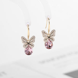 Butterfly-shaped earrings with pink gemstones on a light gray background