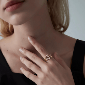 Woman wearing a gold ring with a pink heart-shaped gemstone and a band with shooting star deisgn on a white background