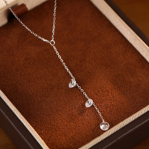 Silver necklace with three droplet pendants on a brown textured surface