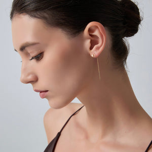 Close-up of a woman wearing a delicate gold earring against a neutral background