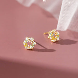 Pair of gold earrings with colorful stones on a pink background