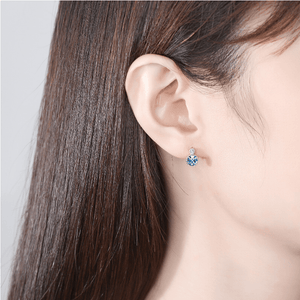 Close-up of an ear wearing a blue gemstone earring with a neutral background