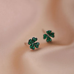 A set of tiny green four leaf clover stud earrings with gold plating on a beige background.