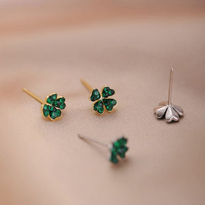 Four pairs of four-leaf clover earrings on a beige background