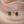 A set of tiny green four leaf clover stud earrings with gold plating on a beige background.