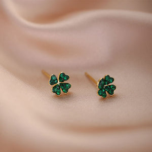 A set of tiny green four leaf clover stud earrings with gold plating on a beige background.