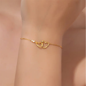 Gold bracelet with interlocking heart design on a wrist against a neutral background