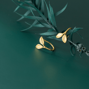 Gold leaf-shaped earrings on a green branch against a dark green background