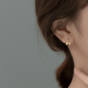Gold butterfly earrings worn by a person with a neutral background