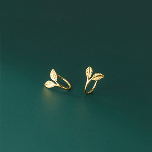 Gold leaf-shaped earrings on a dark green background