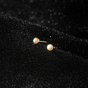 Pair of gold earrings with pearl-like stones on a black textured background