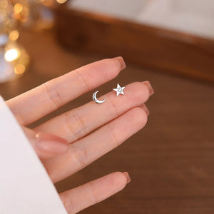 Silver star and moon earrings held between fingers against a blurred background
