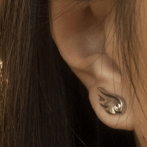 Close-up of an ear wearing a silver earring with a flame design.