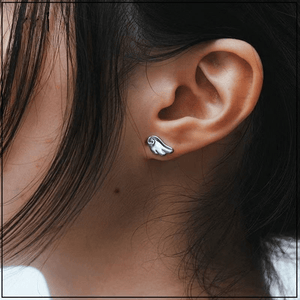 Close-up of an ear wearing a silver earring with a wave design.