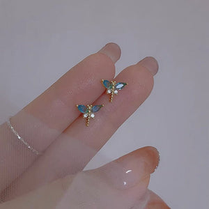 Butterfly-shaped earrings with gemstones on a hand against a plain background
