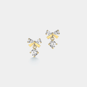 Pair of gold bow-shaped earrings with clear gemstones on a light gray background