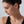 Close-up of a woman wearing a gold earring against a neutral background