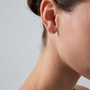 Close-up of a person wearing a gold earring on a plain background