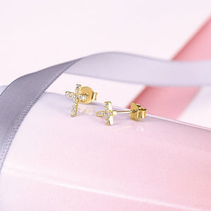 Gold cross earrings on a soft pink and gray fabric background