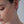 Close-up of a person wearing a small cross earring on a neutral background