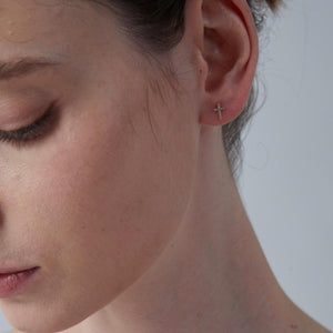 Close-up of a person wearing a small cross earring on a neutral background