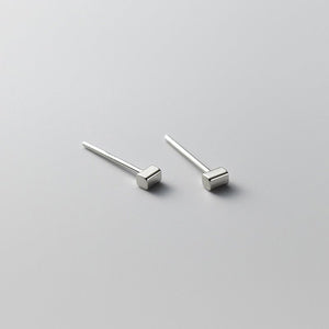 Tiny small cuboid rectangle stud earrings with gold plating on a textured beige background