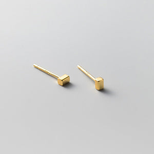 Tiny small cuboid rectangle stud earrings with gold plating on a textured beige background