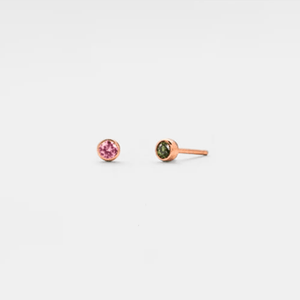 A pair of small custom birthstone stud earrings, with one earring featuring a green birthstone and the other featuring a red birthstone, both set in a solid silver plating.