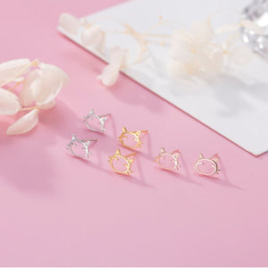 Cat-shaped earrings in silver and gold on a pink surface with floral elements.