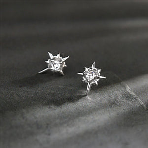Star-shaped silver earrings with clear gemstones on a dark fabric background