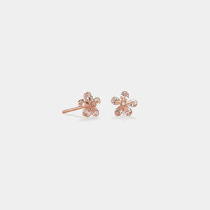 Rose gold flower-shaped earrings on a light gray background