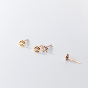Gold and rose gold flower-shaped earrings on a light gray background