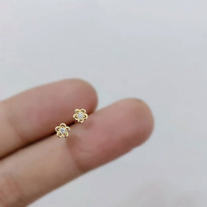Gold flower-shaped earrings held between fingers on a light background