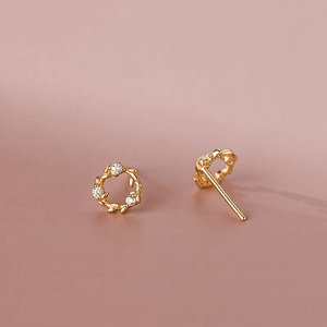 Gold earrings with circular design on a pink background