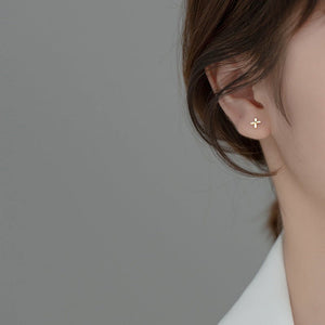 Close-up of an ear wearing a gold cross earring against a neutral background