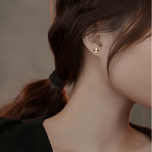 Close-up of a person wearing a gold cross earring with a blurred background