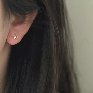 Close-up of a gold floral earring worn by a person with dark hair.